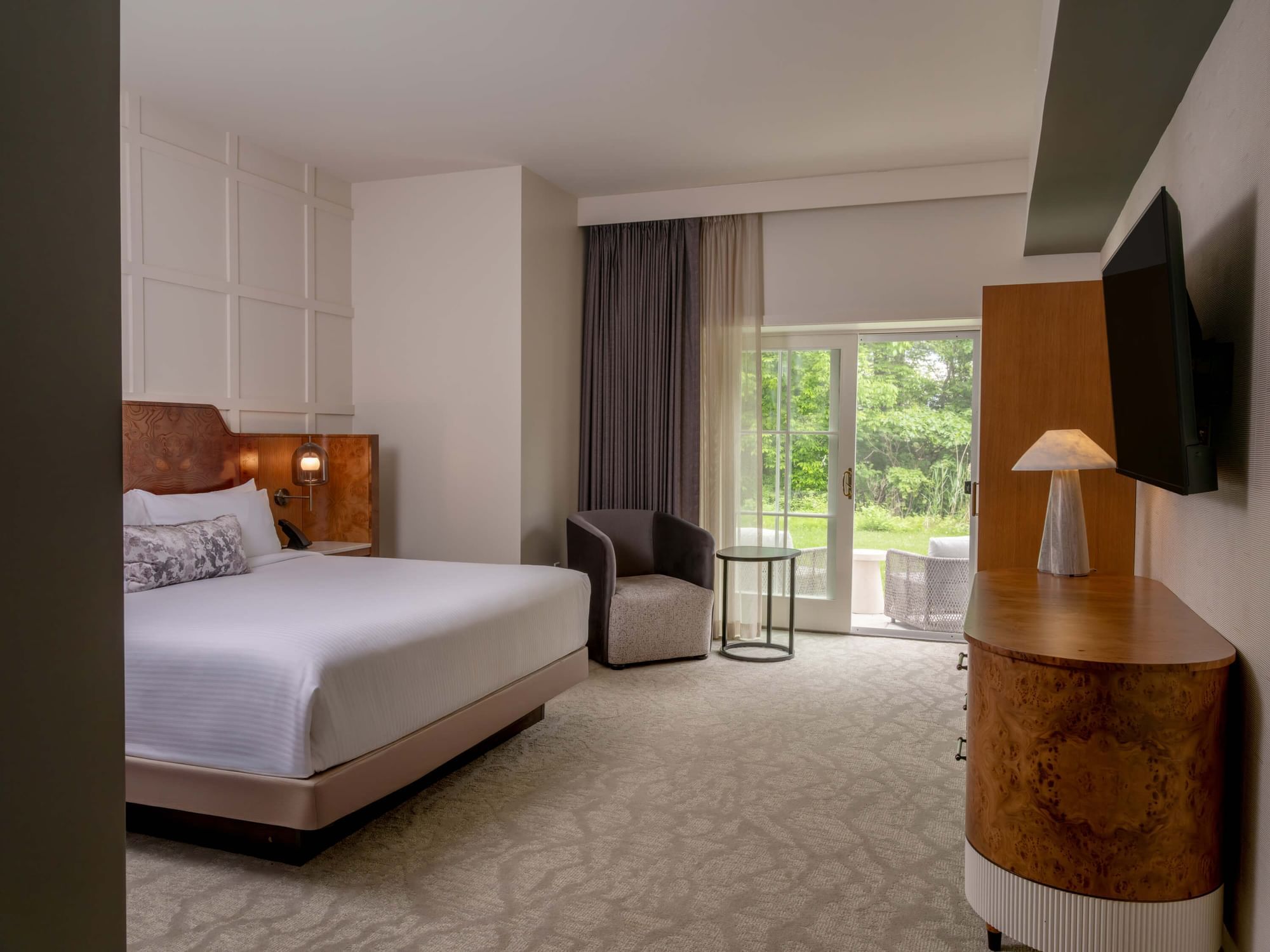 The spa king room with a king size bed, chair, side table, dresser, TV, and glass door leading to a patio.
