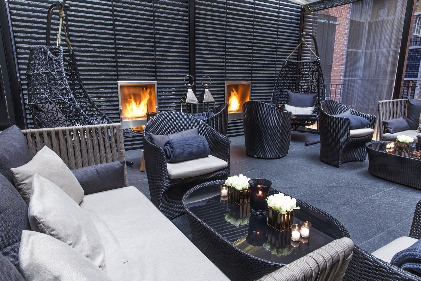 Modern lounge area with wicker chairs and couches, lit fireplaces, and a glass table at The May Fair Hotel London.
