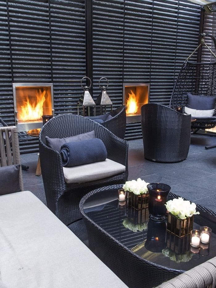 Modern lounge area with wicker chairs and couches, lit fireplaces, and a glass table at The May Fair Hotel London.