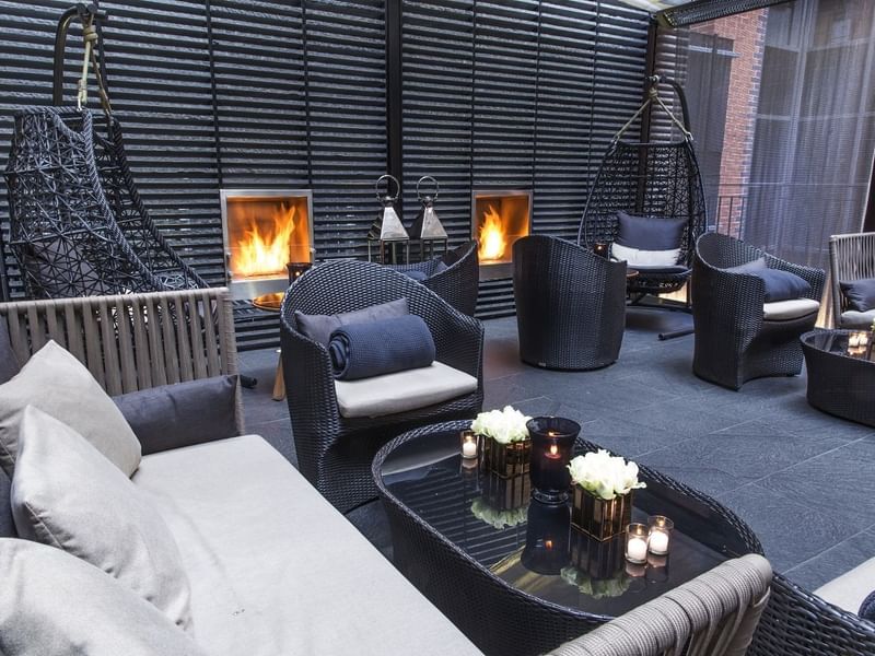 Modern lounge area with wicker chairs and couches, lit fireplaces, and a glass table at The May Fair Hotel London.