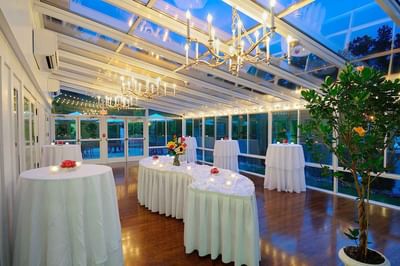 Solarium event room with a glass ceiling and chandeliers, featuring high tables set for reception at The Simsbury Inn