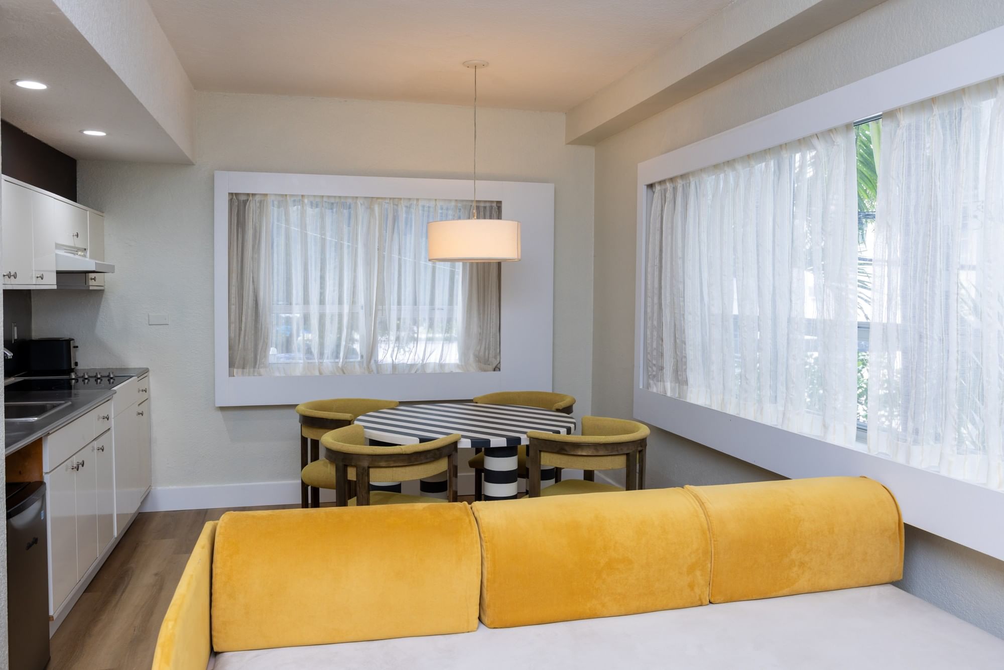 A wide view of a furnished living room with a kitchenette, dining table, and yellow sofa.