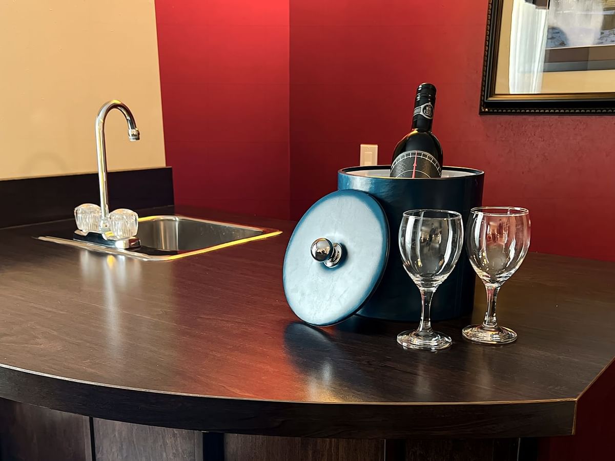 A bottle of wine, two glasses, and a sink on the table