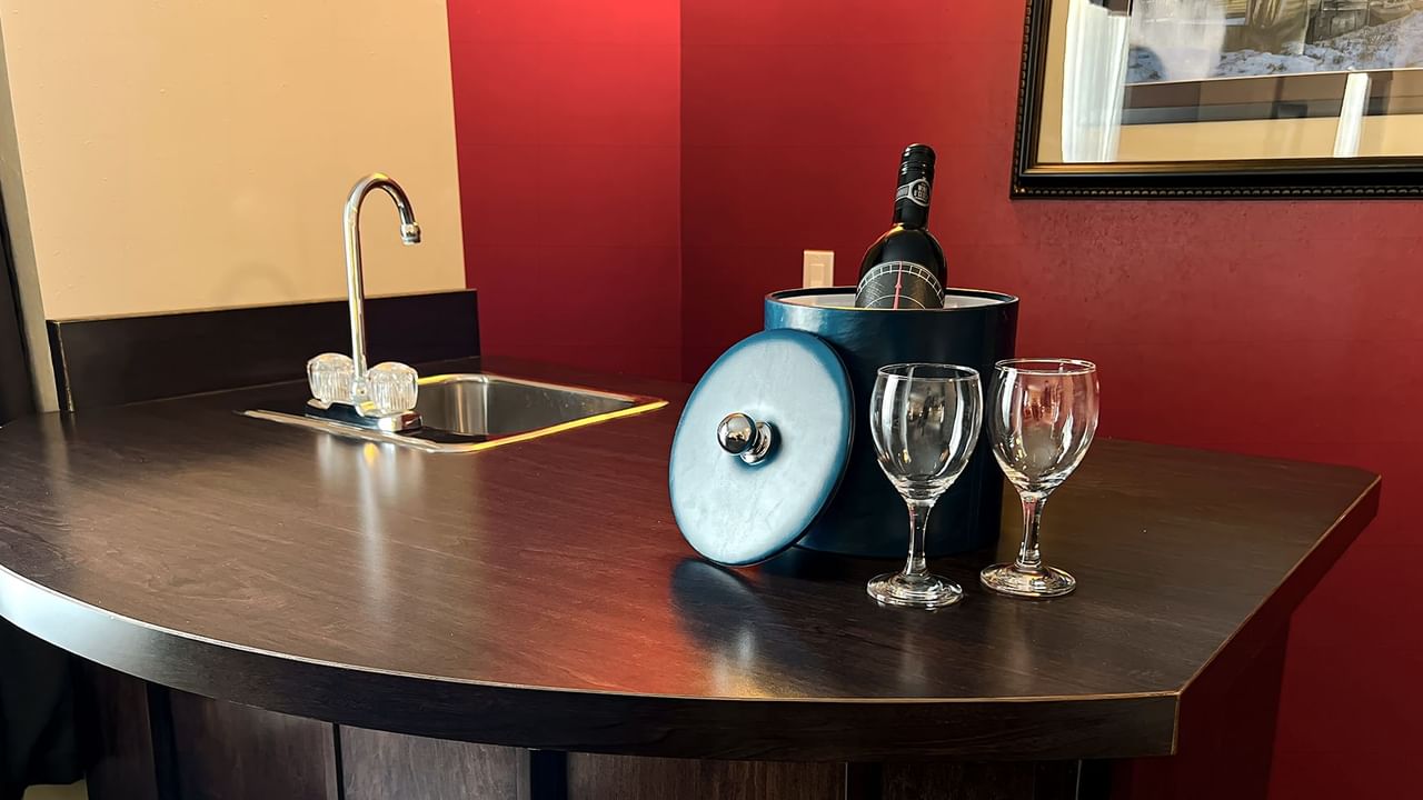A bottle of wine, two glasses, and a sink on the table