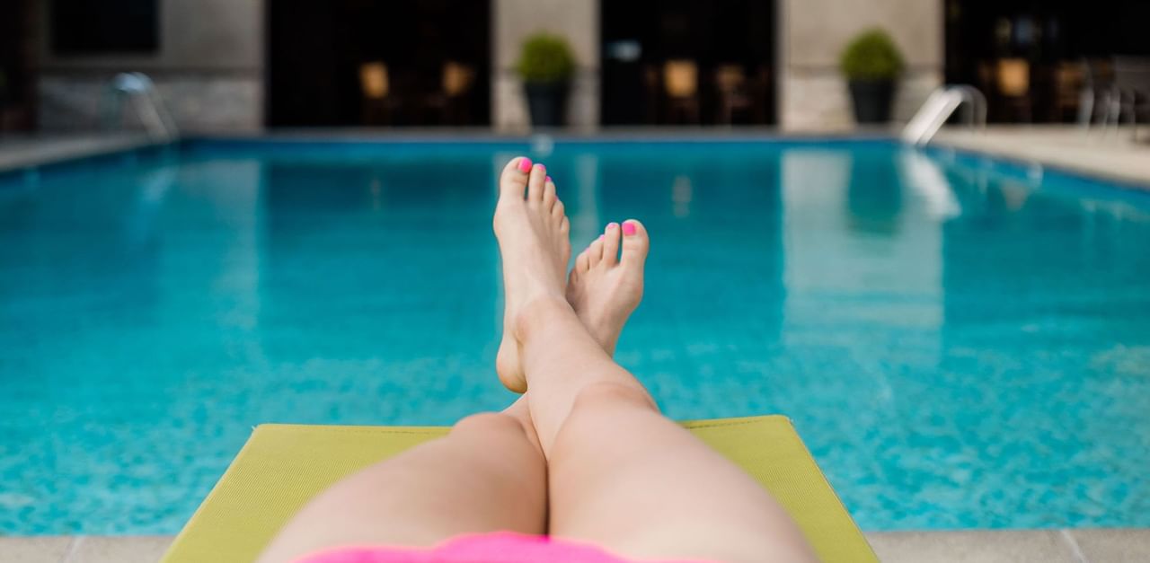 women's feet resting on a lawn chair by the courtyard pool