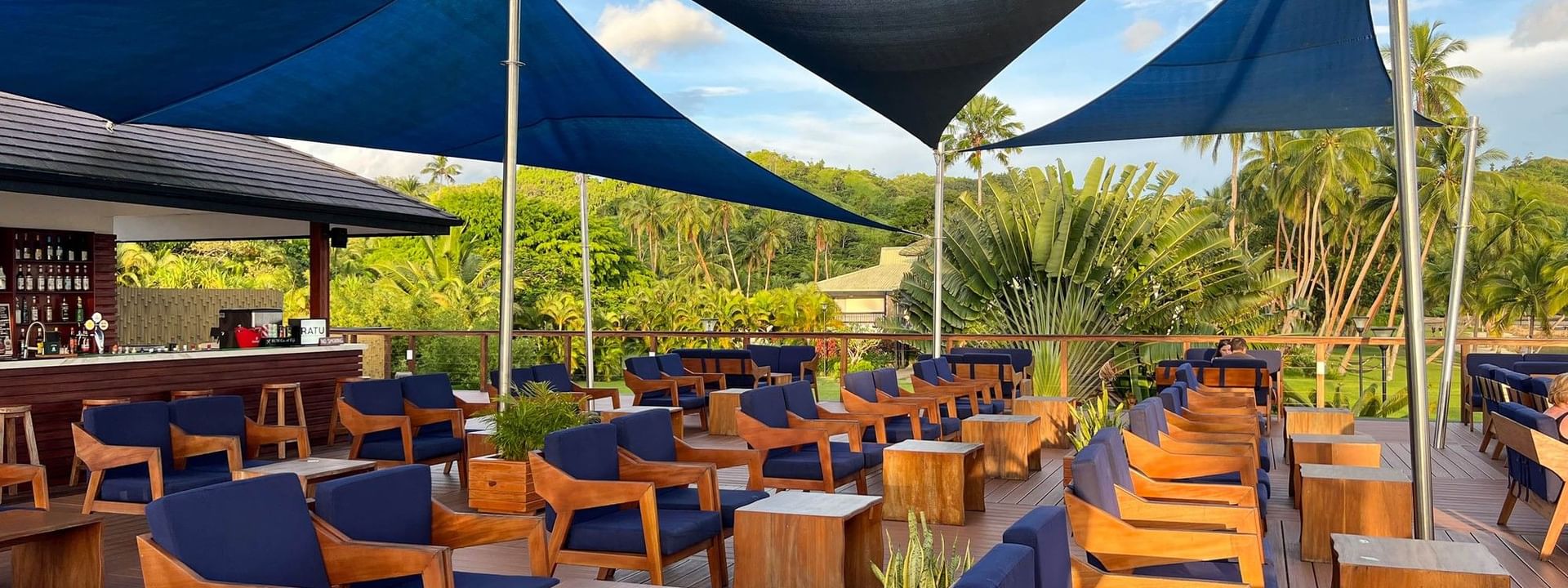 Wooden lounge chairs with blue cushions and canopy shades on a deck at Sunset Bar in Korolevu at The Naviti Resort - Fiji