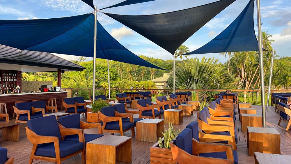 Wooden lounge chairs with blue cushions and canopy shades on a deck at Sunset Bar in Korolevu at The Naviti Resort - Fiji.