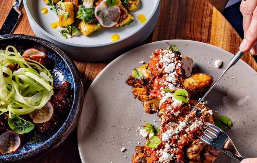 Three dishes with various ingredients and utensils on a wooden table at Paradox Vancouver