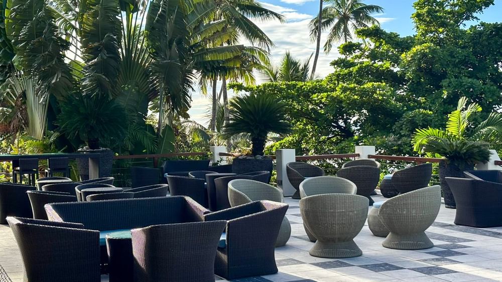 Outdoor seating area with wicker chairs and tables surrounded by lush greenery at Warwick Fiji Resort and Spa.