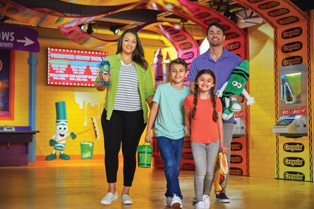 A mom, dad, and two kids walk through the colorful Crayola Experience carrying merchandise. 
