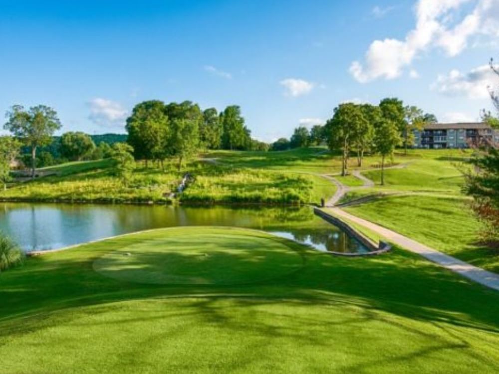 Pointe Royale Golf Course with a round putting green near a pond and distant buildings near Branson Hillside Hotel