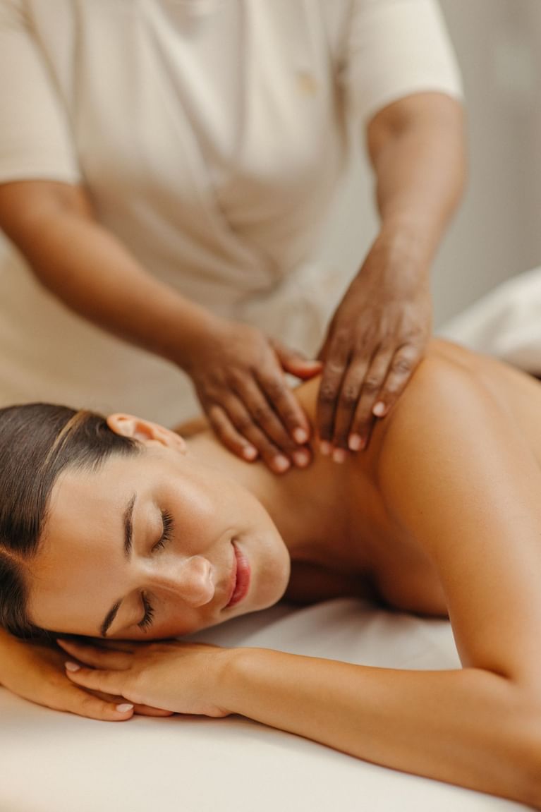 Woman on massage table receiving shoulder massage from therapist with blurred background.
