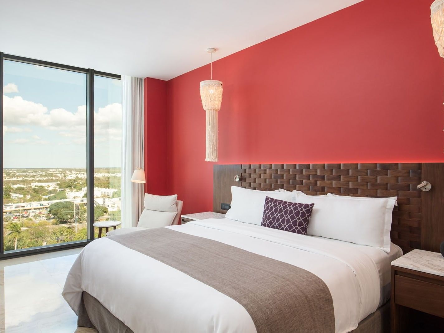 King Deluxe Bed featuring a bold red wall, woven headboard, and floor-to-ceiling city views at Camino Real Merida