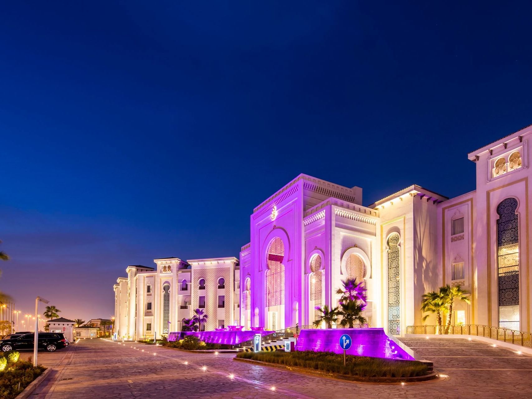 Illuminated purple building with a driveway and a black car parked on the side at night.