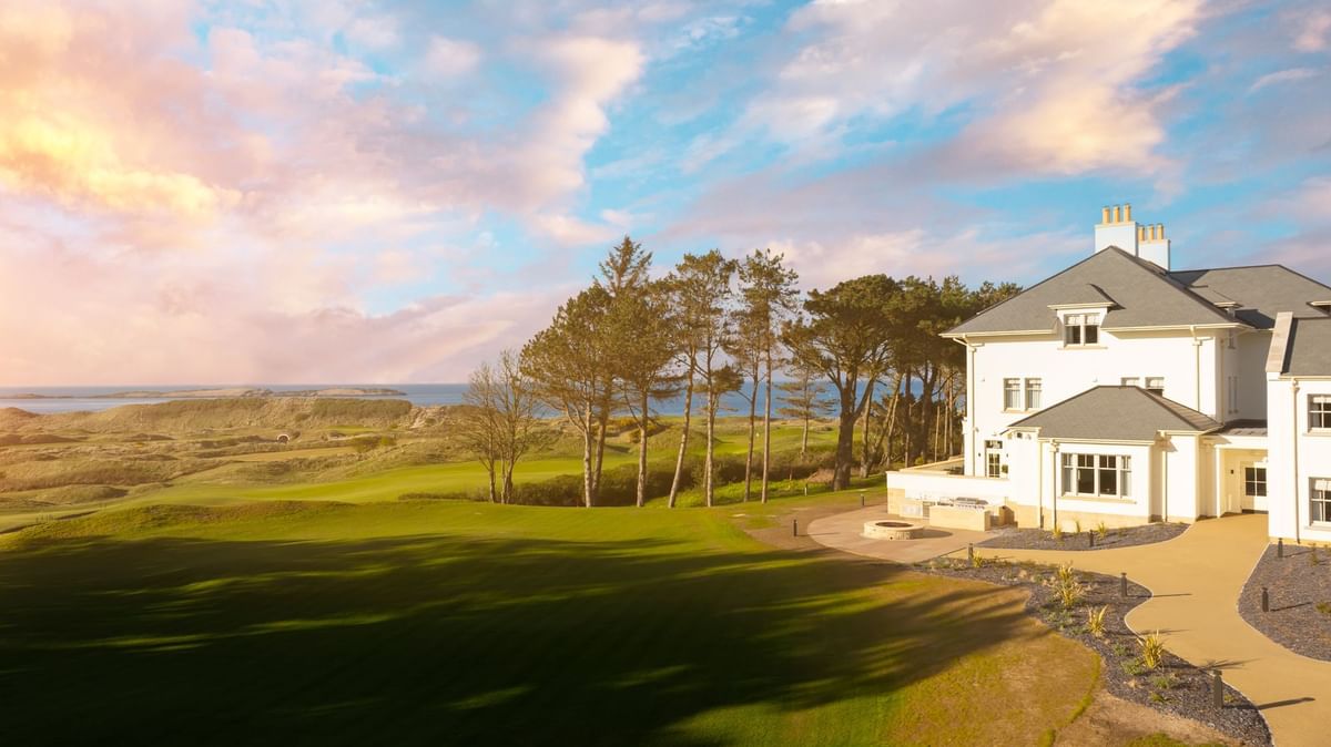 A dramatic sunset over the golf course and sand dunes near Dunluce Lodge, with a view of the white building