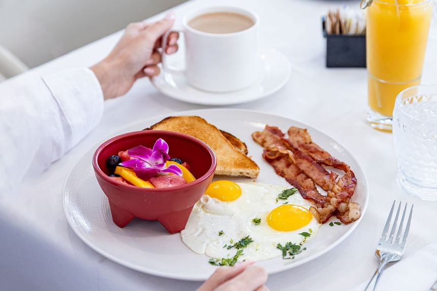 Person having breakfast with eggs, bacon, toast, fruit bowl, coffee, and juice at The Savoy Hotel & Beach Club