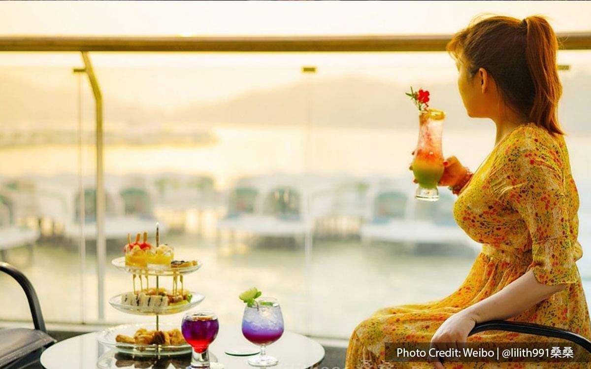 A woman enjoying beautiful sunset and beverage at Lexis Hibiscus Resort's balcony