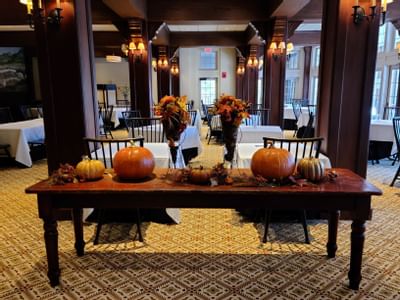 Wooden table decorated with orange pumpkins and autumn leaves between black chairs in dining room at The Simsbury Inn