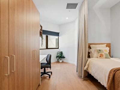 Tidy single bedroom with wooden bed, desk, and large closet at UniLodge Brisbane City.