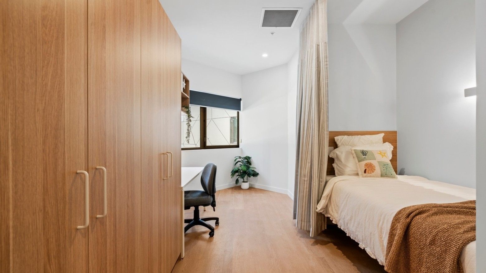 Tidy single bedroom with wooden bed, desk, and large closet at UniLodge Brisbane City.