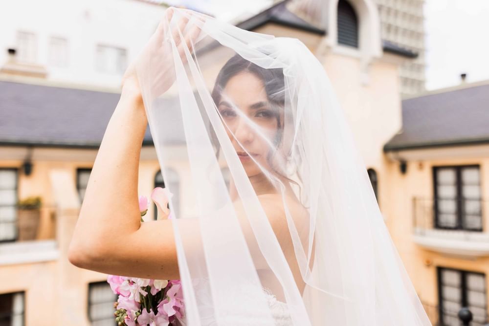 Beautiful bride peeking from behind her veil, holding a bouquet at the El Prado Hotel