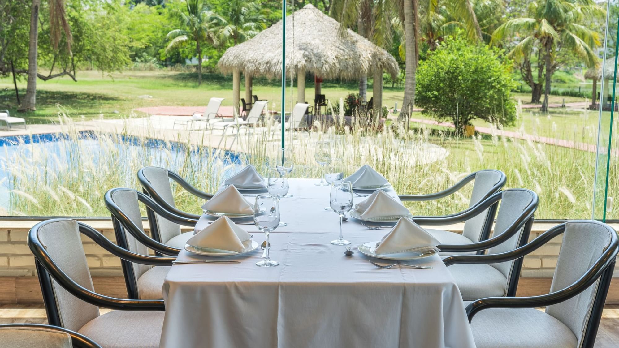 Elegant dining table overlooking a lush garden and pool with a thatched gazebo at Fiesta Inn Tampico