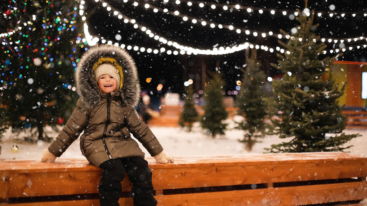 kid sitting with holiday lights on trees