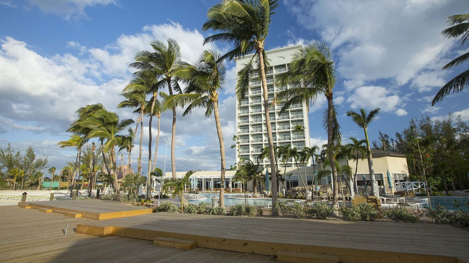 Wooden deck by a pool area under palm trees surrounding a white hotel tower near Warwick Paradise Island Bahamas