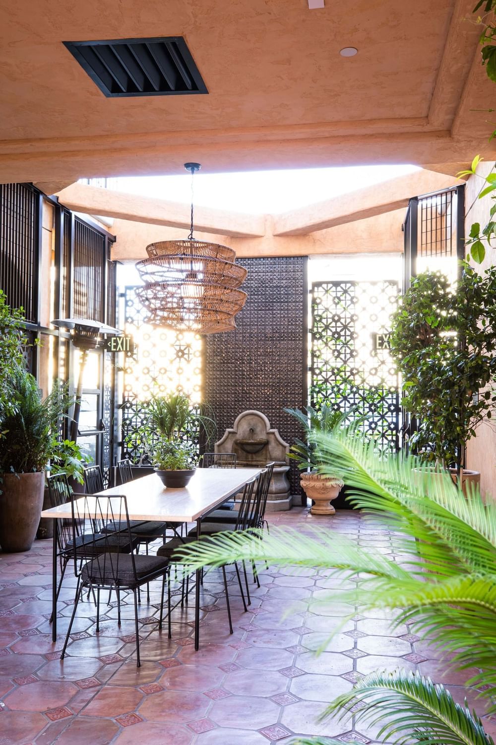 Outdoor dining area featuring a long table, a fountain, and lush potted plants at El Prado Hotel