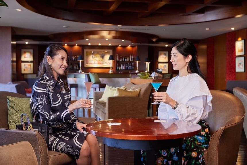 Two people sitting at a table with cocktails in Marina Bar & Restaurant at Grand Park Otaru