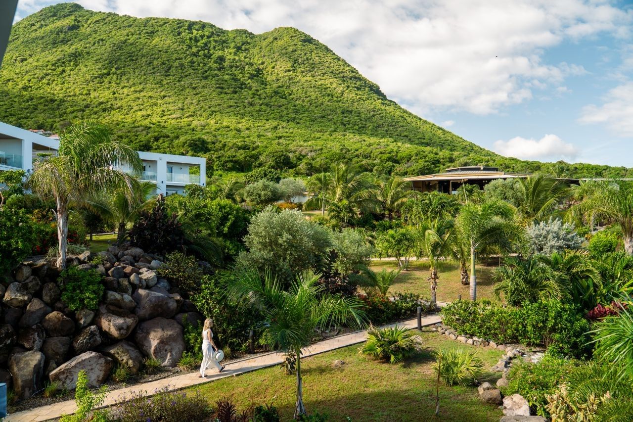 Guest walking along a paved garden path past tropical palm trees with a scenic mountain view at Golden Rock Resort