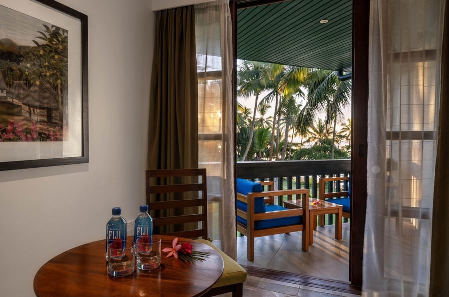 Wooden table with water bottles by a chair under a framed art piece in Warwick Deluxe Rooms at Warwick Fiji Resort and Spa