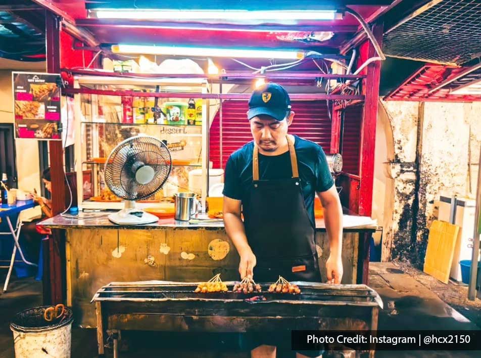 Person grilling meat skewers on the BBQ, Malaysian street food tour near Imperial Lexis Kuala Lumpur