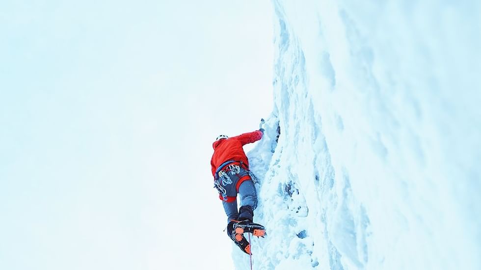 Climber scaling a steep icy slope with climbing gear near Falkensteiner Hotel Kronplatz