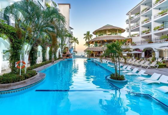 Sparkling blue swimming pool flanked by palm trees and white lounge chairs at Playa Los Arcos Beach Resort & Spa