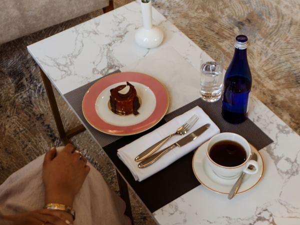 Small chocolate cake by a cup of coffee on a marble table in Al Maha Café at Cantonal Hotel by Warwick Riyadh