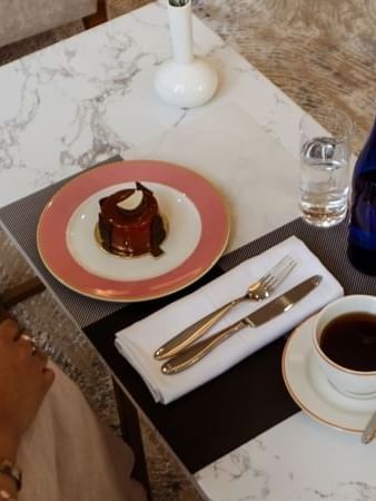 Small chocolate cake by a cup of coffee on a marble table in Al Maha Café at Cantonal Hotel by Warwick Riyadh