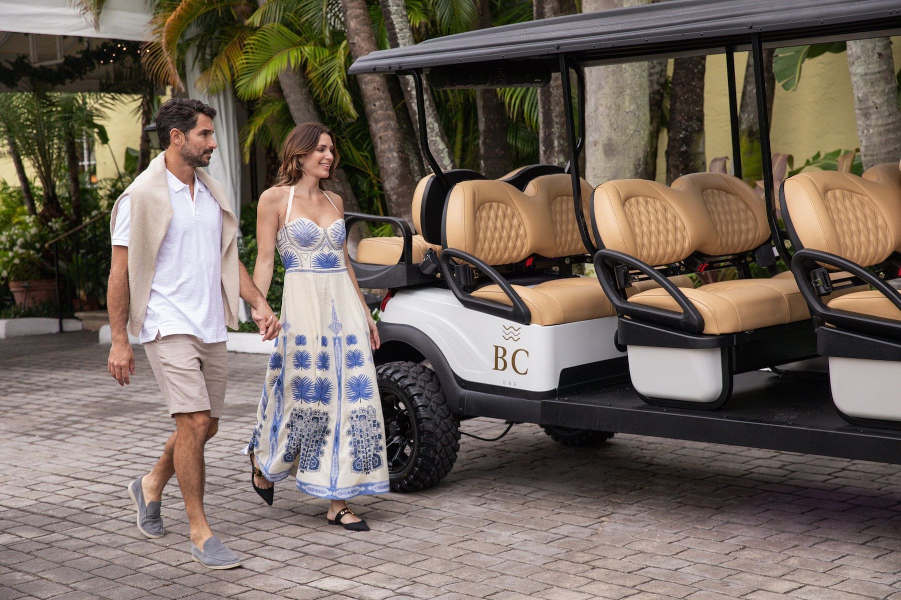 Couple walking hand in hand next to a black and white golf cart with beige seats.