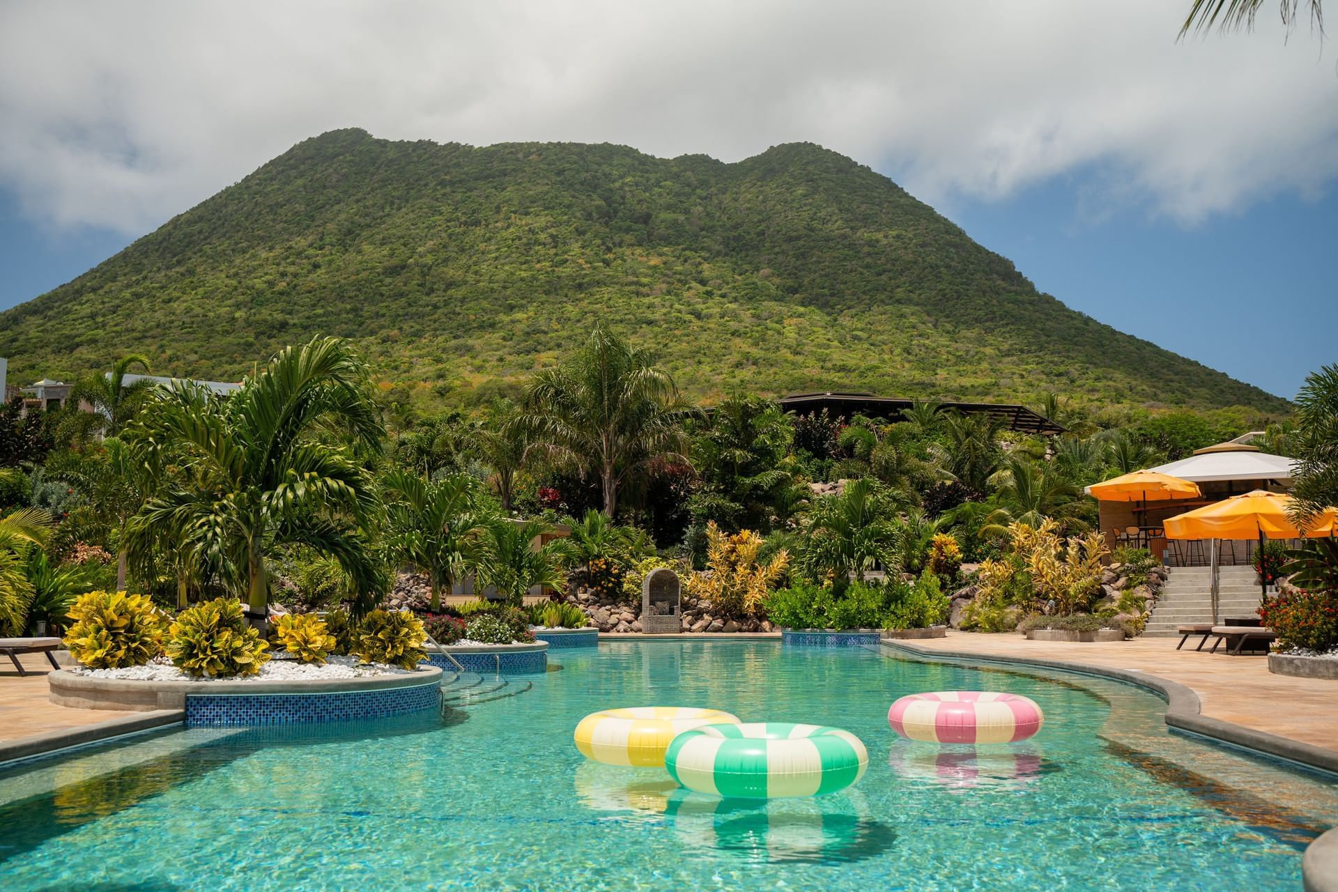 Hummingbird Pool omringd door groen, met zwembanden en een majestueuze berg op de achtergrond bij Golden Rock Resort