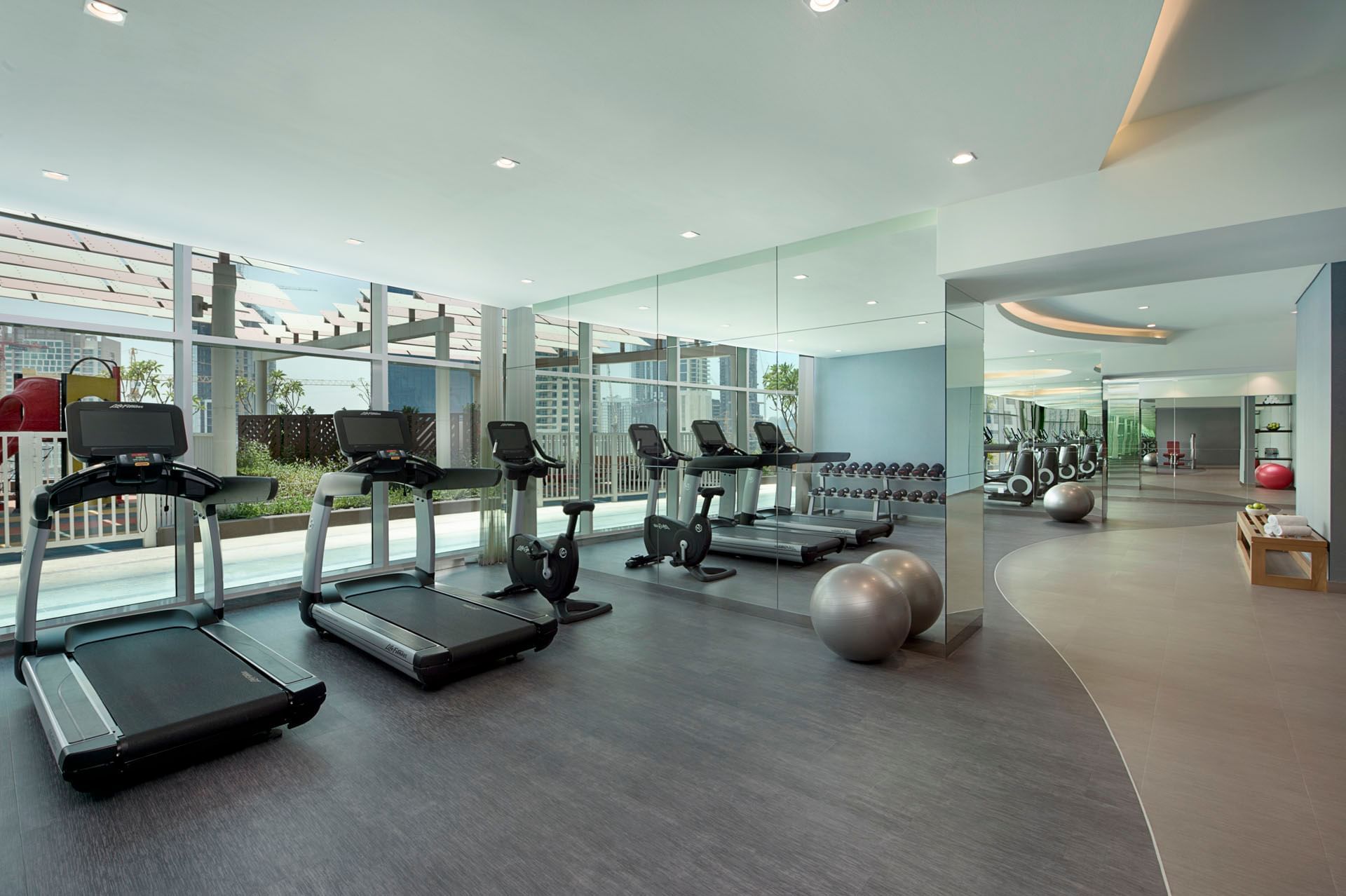 A well-lit gym with treadmills by the large windows in The Distinction Gym at DAMAC Maison Distinction