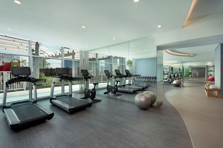 A well-lit gym with treadmills by the large windows in The Distinction Gym at DAMAC Maison Distinction