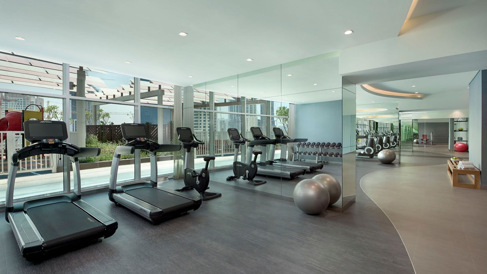 A well-lit gym room with treadmills in The Distinction Gym at DAMAC Maison Distinction