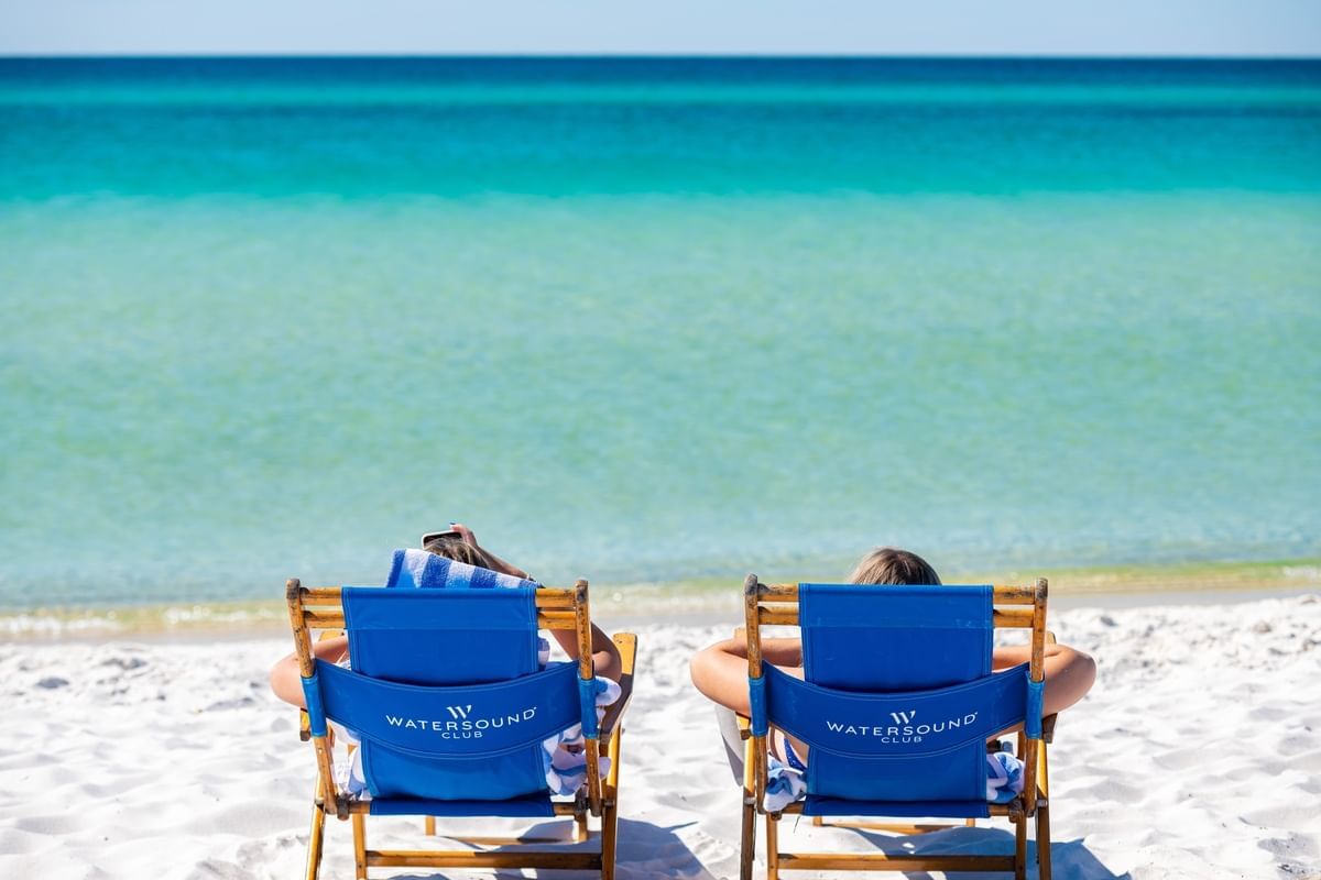 Two people relaxing on loungers by the beach on a sunny day near Camp Creek Inn