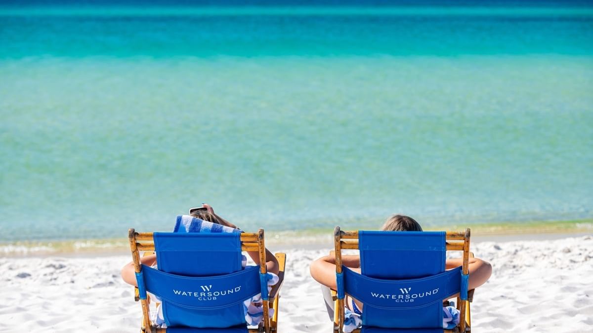 Two people lounging in Watersound Club beach chairs on a beautiful day at the Beach Club
