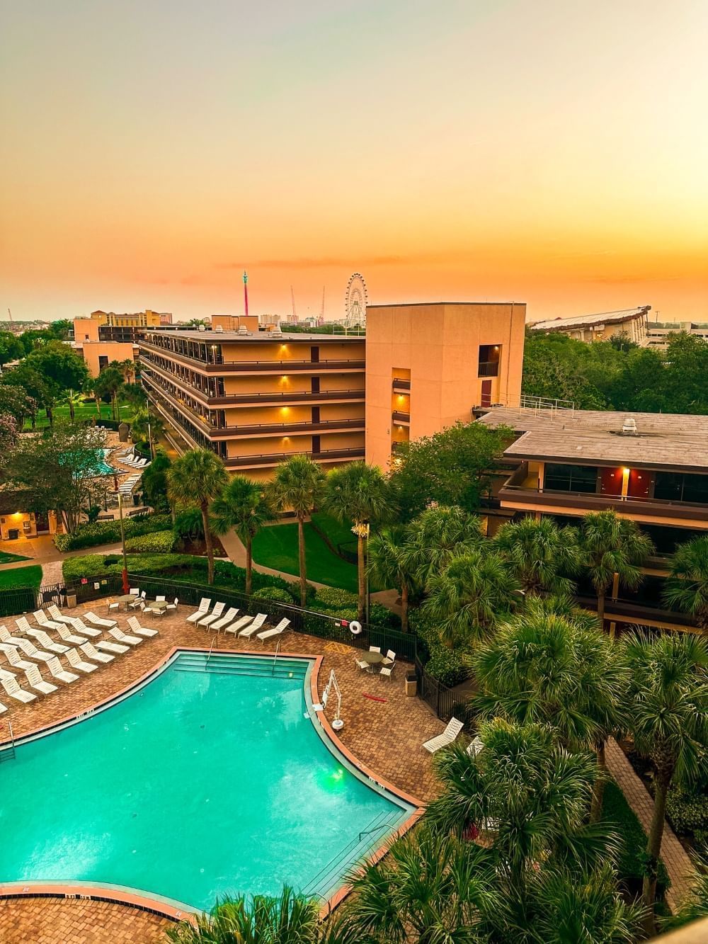 An ariel view of Rosen Inn at Pointe Orlando, a family-friendly hotel in Orlando, featuring a sparkling blue pool and a cityscape background.