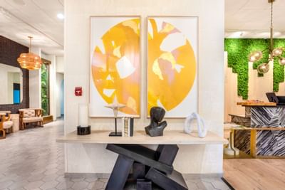 Modern lobby at The Riverwalk Plaza Hotel featuring vibrant yellow art, sculptures, and earthy decor in a stylish setting