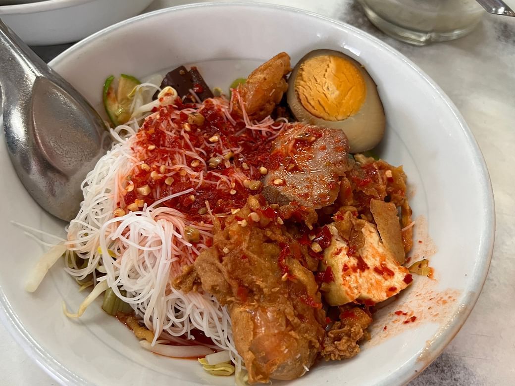 Bowl of spicy Thai noodles with chicken, a hard-boiled egg, and fried tofu, served at Hop Inn Hotels