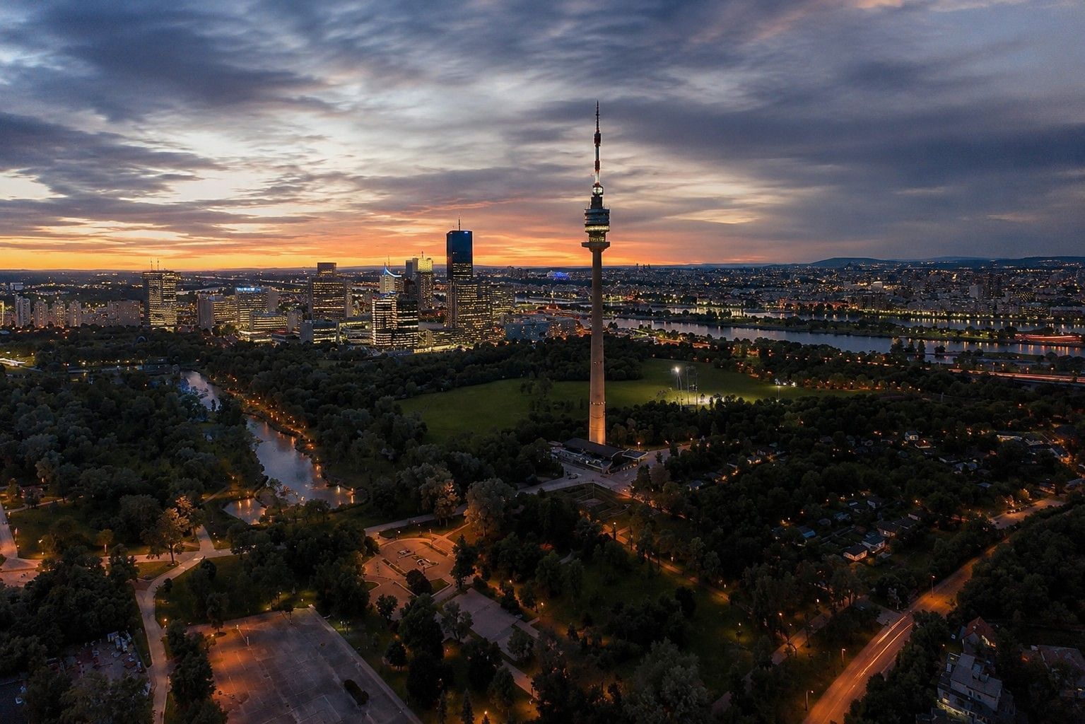 Donauturm in Wien bei Abendstimmung mit beleuchteter Skyline, Donau und grüner Parklandschaft