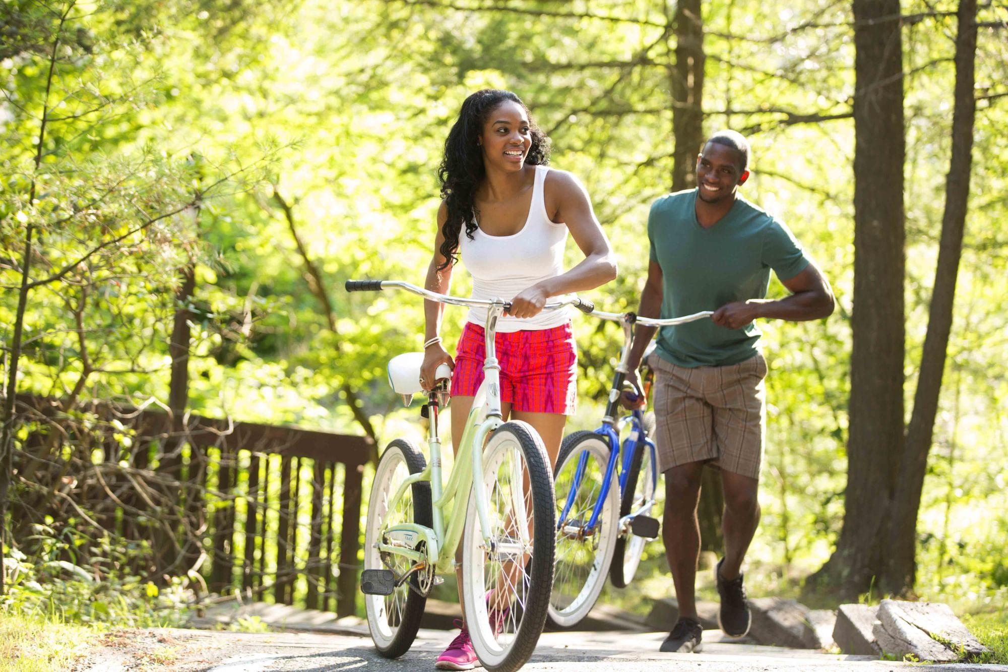 Couple walks alongside with a bicycle in a lush, sunlit forest near Cove Pocono Resorts