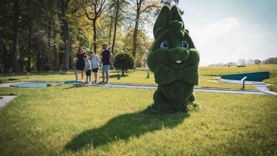 A family stands on a golf course with a large green, animated tree mascot in the foreground.